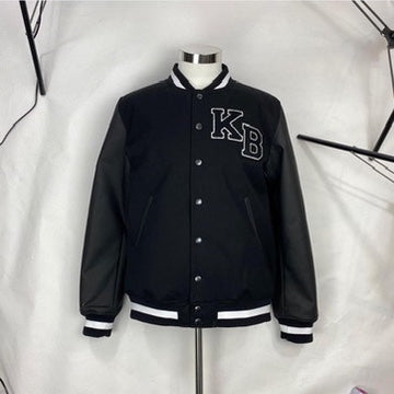 A black varsity jacket displayed on a mannequin against a plain background. The jacket features leather sleeves, striped cuffs, and collar, with large KB lettering on the chest.