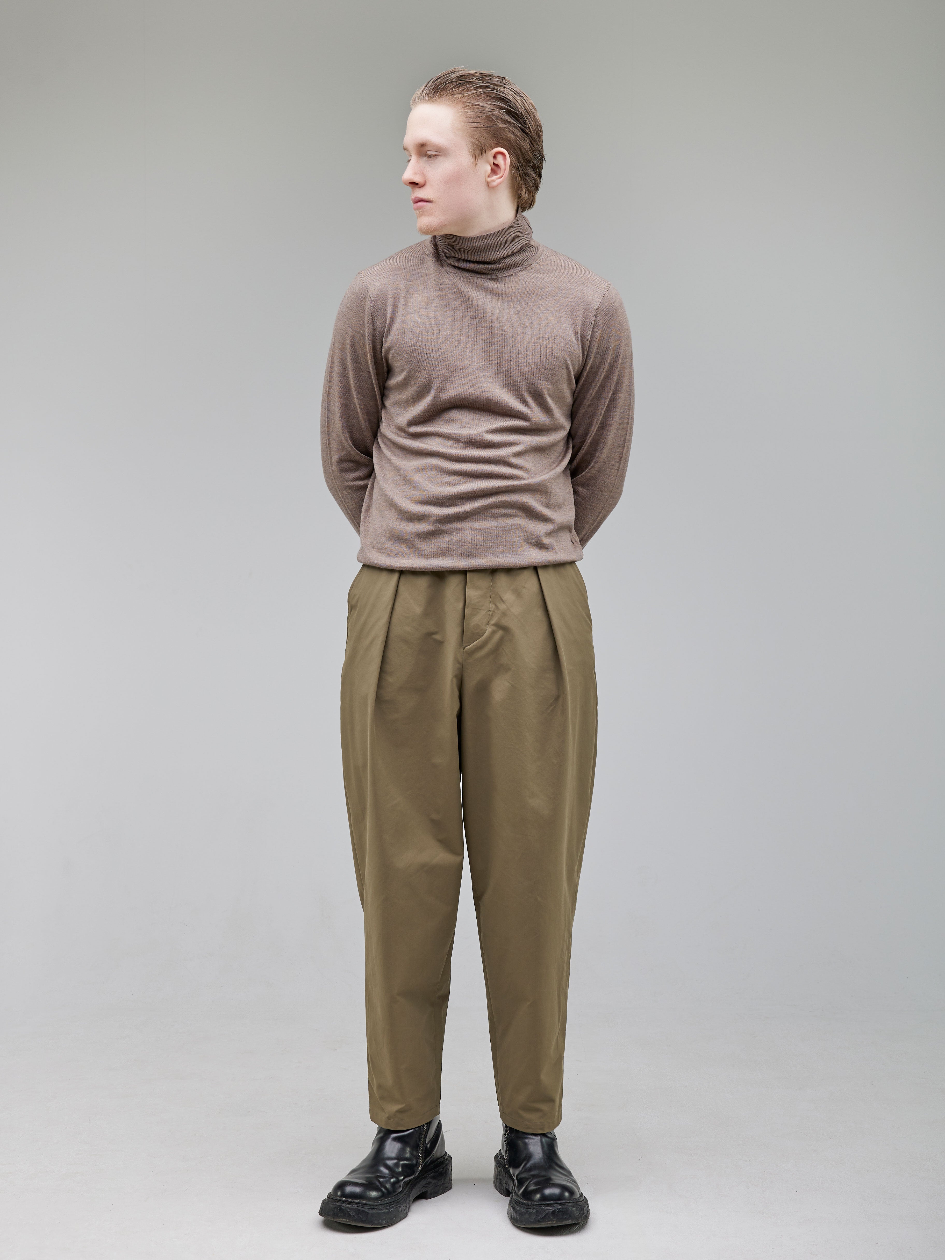 Tapered trousers with a rounded leg, featuring front pleats and a tailored waistband with button closure.