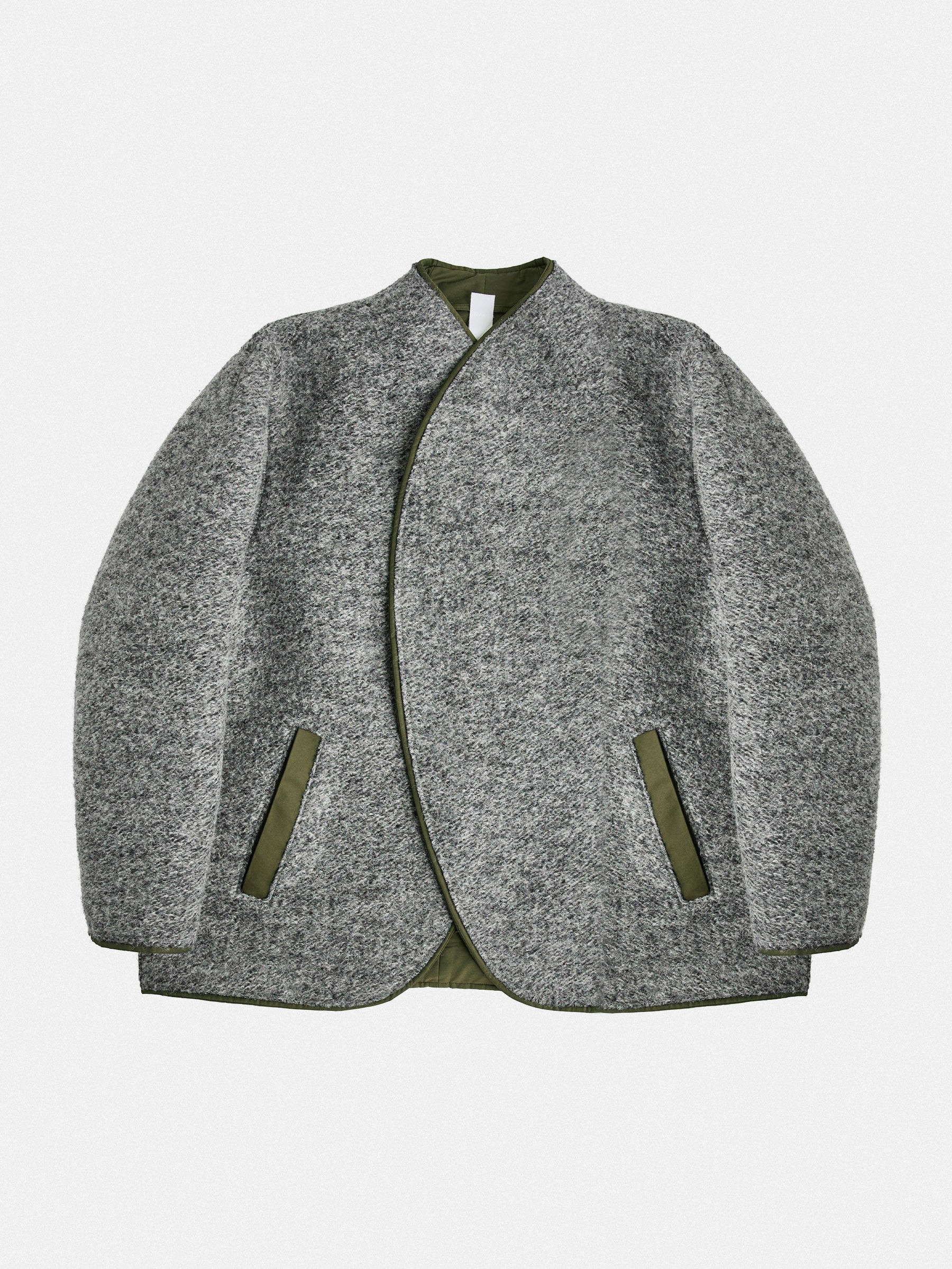 A versatile reversible jacket in grey/dark navy melange, featuring contrasting welt pockets. Its collarless design is shaped with darts for a refined neckline and structured shoulders. The interior mirrors the construction with added patch pockets. Precision piping unites both layers, reinforcing durability and design.

Outer: 80% Wool, 20% Polyester

Reverse: Cotton gabardine (58% Cotton, 38% Polyamide) with a light PU finish in army green

Closure: 8mm gunmetal zipper
