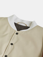 Close-up of the Hazelnut College Jacket by gabrielstunz, showcasing a beige design with black buttons that evoke a classic collegiate style. A white collar and hanging loop complete the Ivy League tradition look, perfectly displayed on a plain white background.