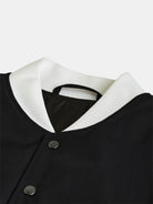 Close-up of the gabrielstunz "Silverskin" College Jacket Black with a transparent coating against a light background. Crafted with European expertise, this jacket features a white ribbed collar and sleek black fabric adorned with metal snap buttons. The interior lining is visible beneath the collar, highlighting its refined details.