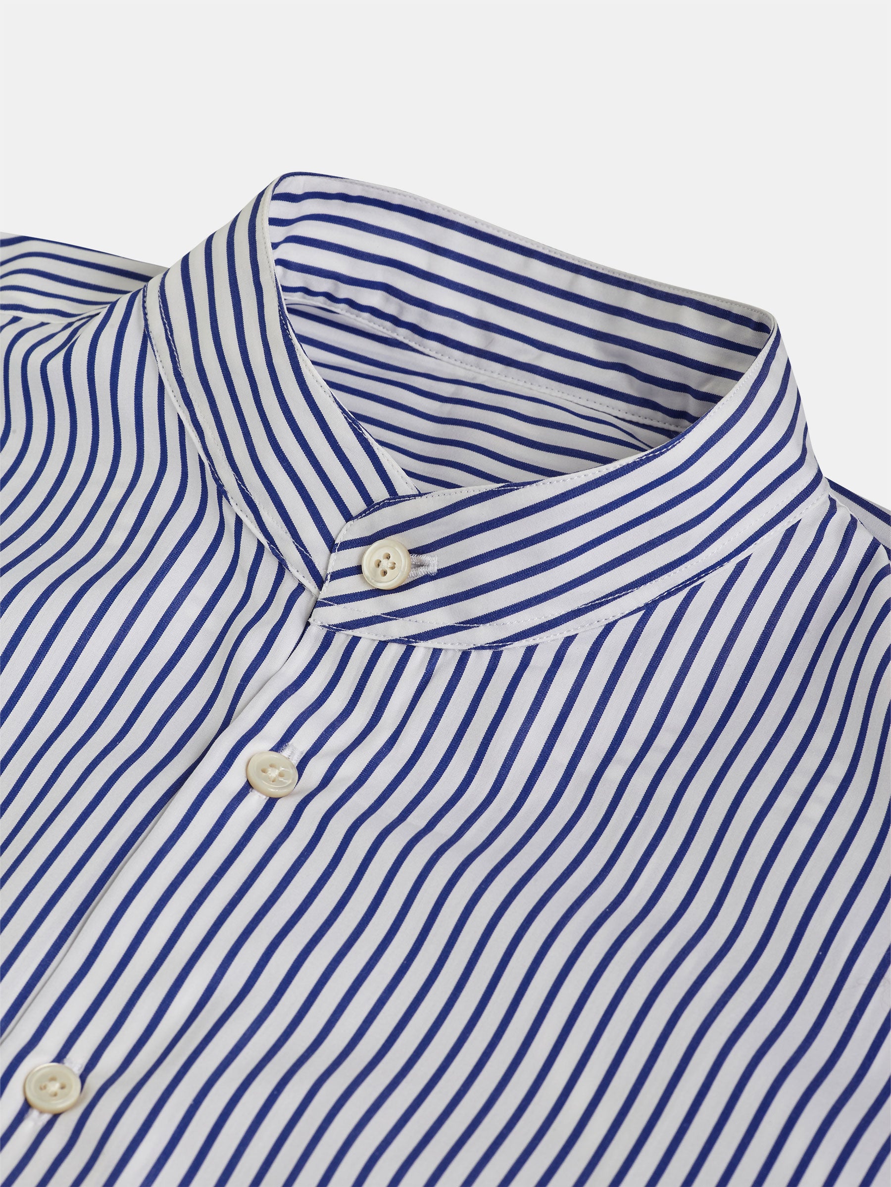 Close-up of a blue and white striped POCKETPARACHUTE® Shirt with Mao collar by gabrielstunz, showcasing its neatly buttoned design. The evenly spaced vertical stripes offer a classic, clean aesthetic, while elegant mother-of-pearl buttons add a touch of sophistication.