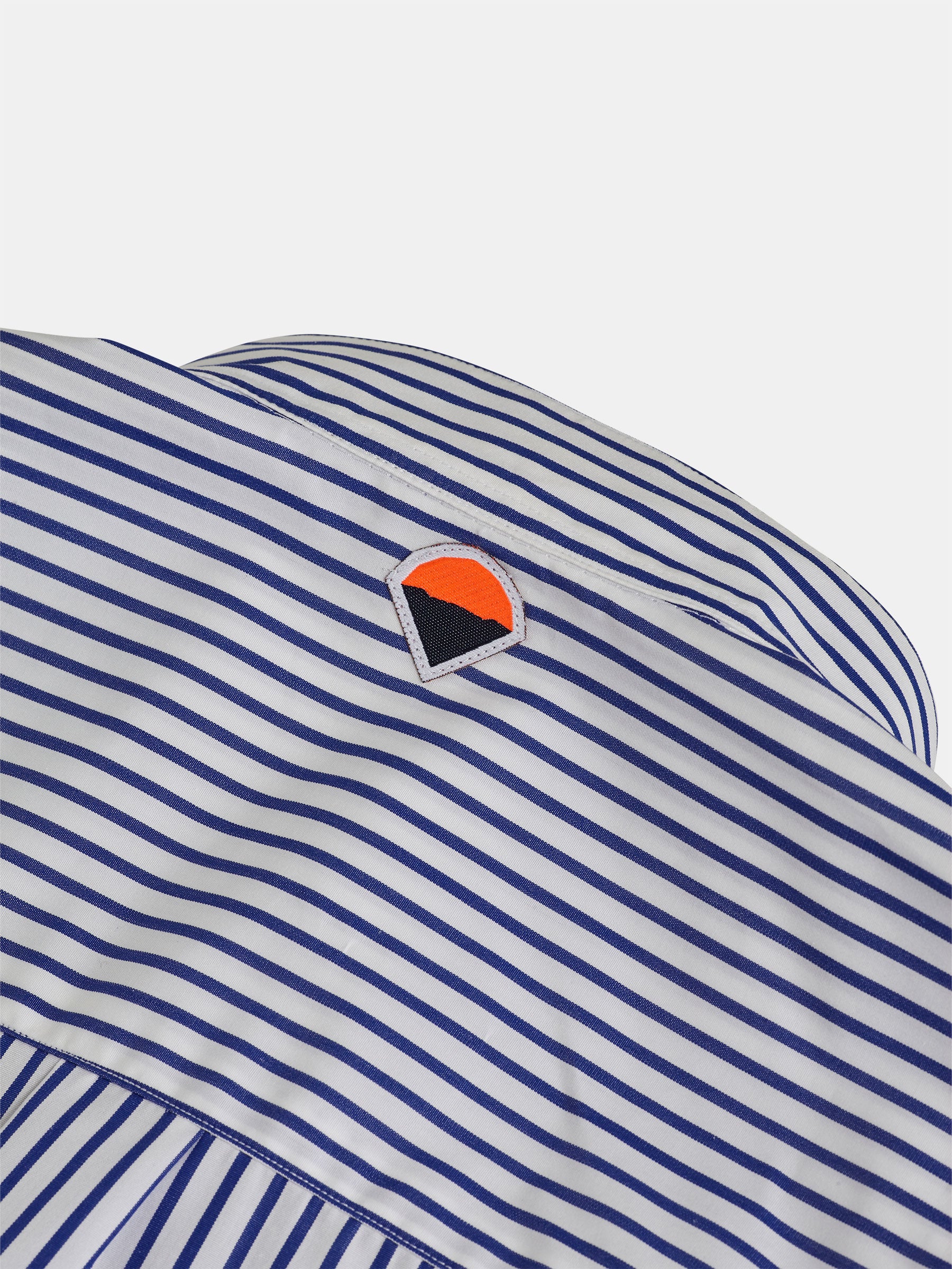 Close-up of a white and blue striped fabric featuring an embroidered logo with an orange semicircle above a black triangle. The gabrielstunz POCKETPARACHUTE® Shirt with Mao Collar, complemented by mother-of-pearl buttons, exudes subtle elegance and character.