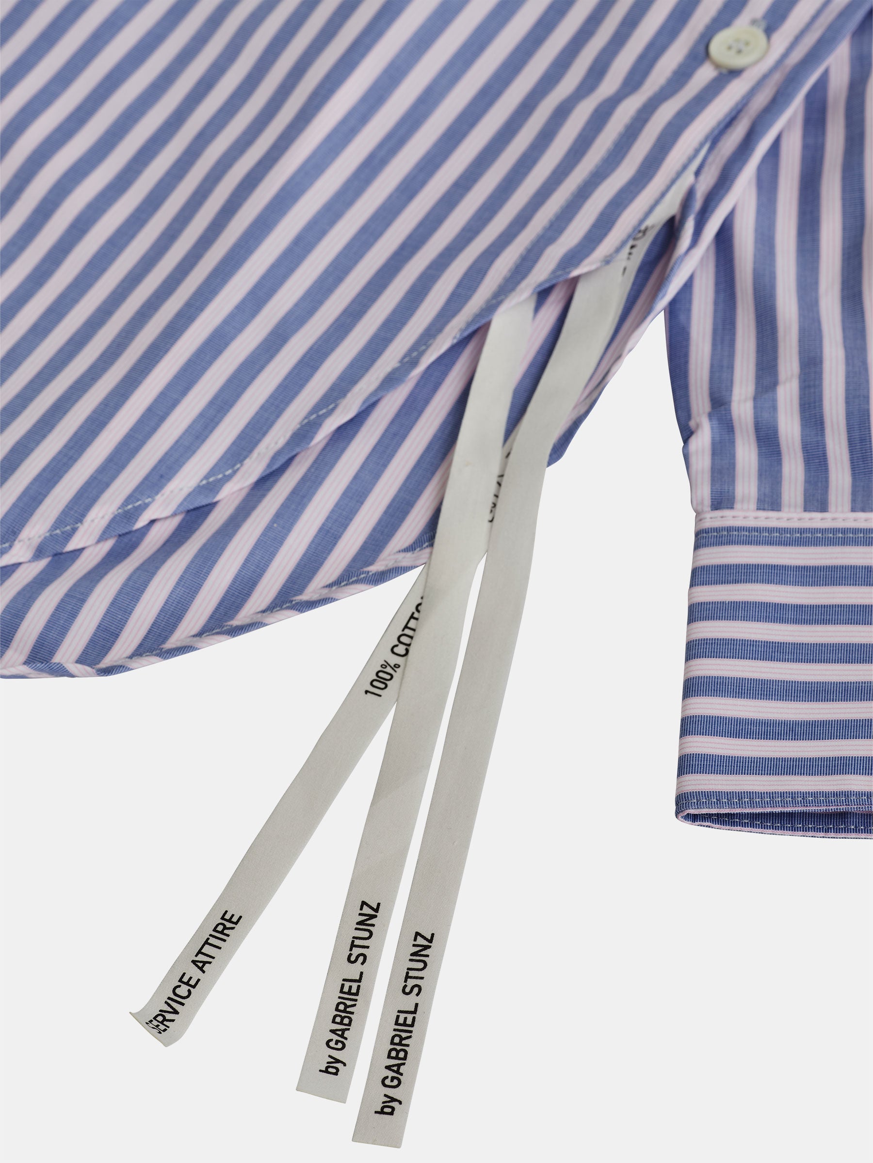 Close-up of an oversized Mao collar shirt by gabrielstunz, featuring light blue with pink stripes and contemporary design elements like long white tags with text. The buttoned cuffs enhance the premium fabric's smooth and neatly tailored appearance.