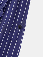 An image showcasing a detailed view of the Oversize Mao Collar Shirt Navy with White Pinstripes by gabrielstunz, highlighting the elegant navy luxury fabric adorned with white vertical pinstripes and accented by a black side button. The material is slightly sheer, revealing the intricate texture and stitching characteristic of this oversized shirt.