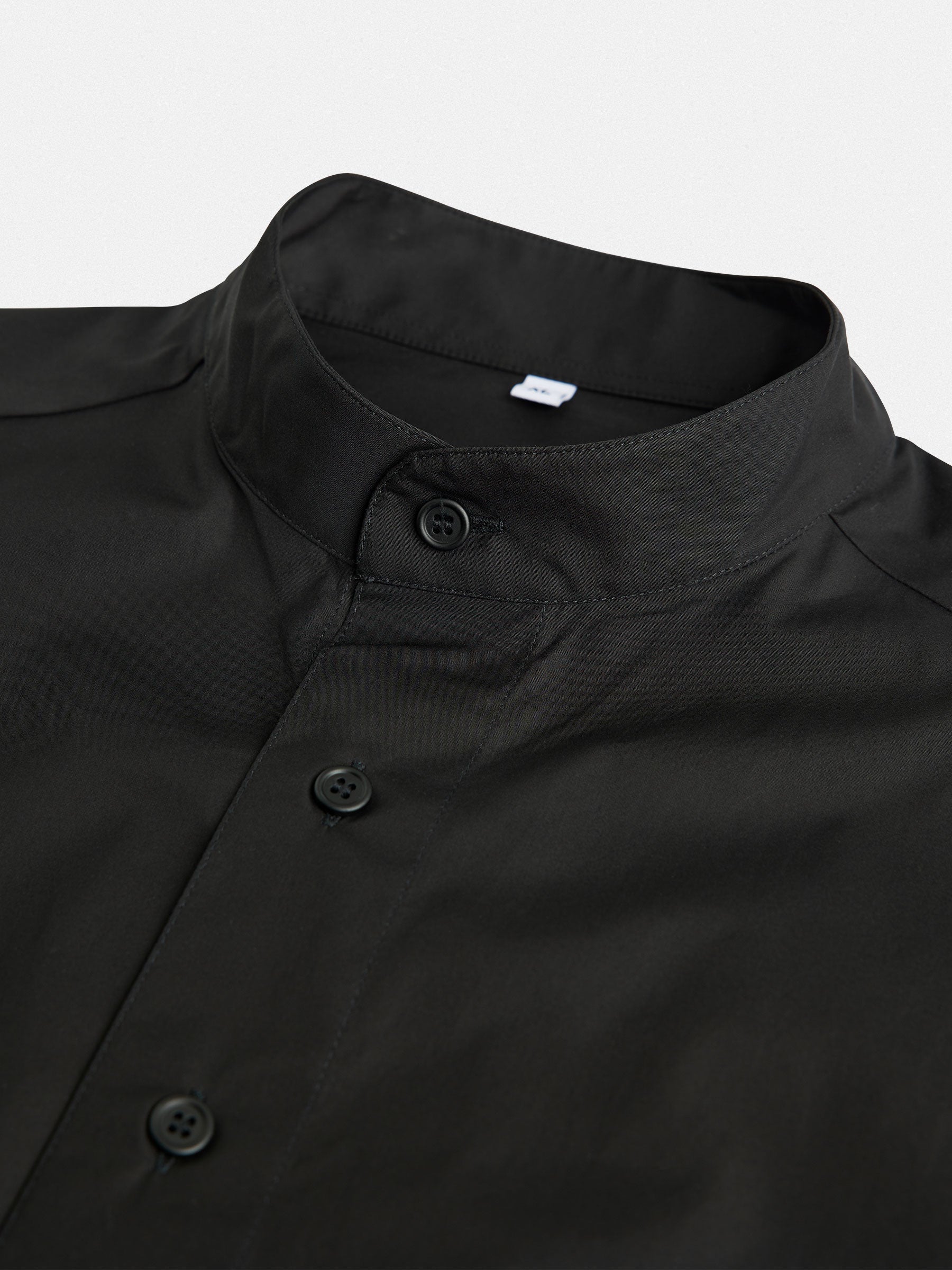 Close-up of an Oversized Cotton Shirt from gabrielstunz, featuring a black button-up design with a mandarin collar. Crafted from premium cotton, the sleek fabric and three visible buttons are accentuated against a plain white background, showcasing its European craftsmanship.