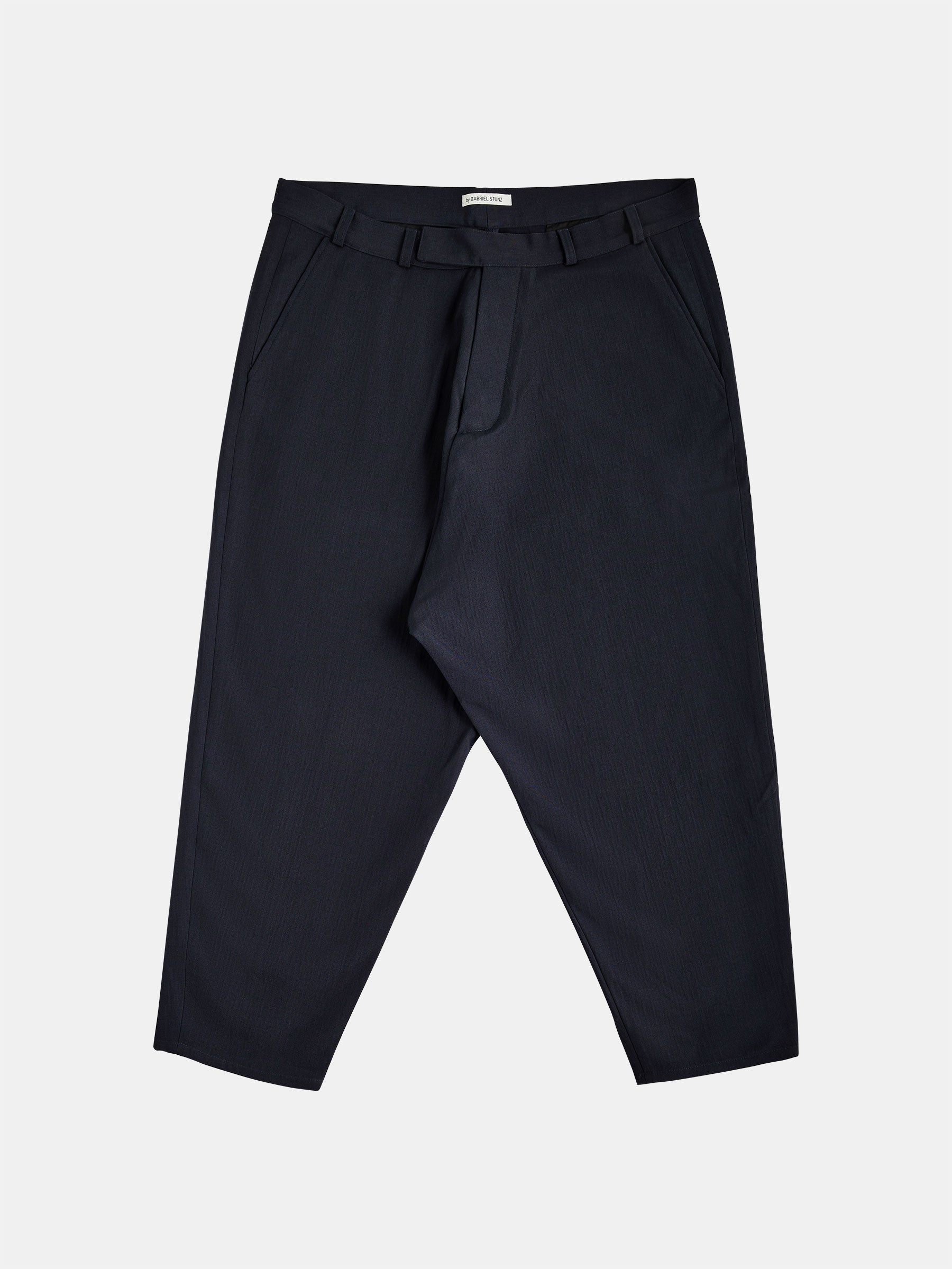 Dropped Crotch Wide-Cut Trousers by gabrielstunz are presented in a black wool and silk blend with a tapered leg design, complete with a waistband and belt loops. They feature a front zipper closure and vintage-style corozo buttons, along with side pockets, elegantly displayed against a plain white background.