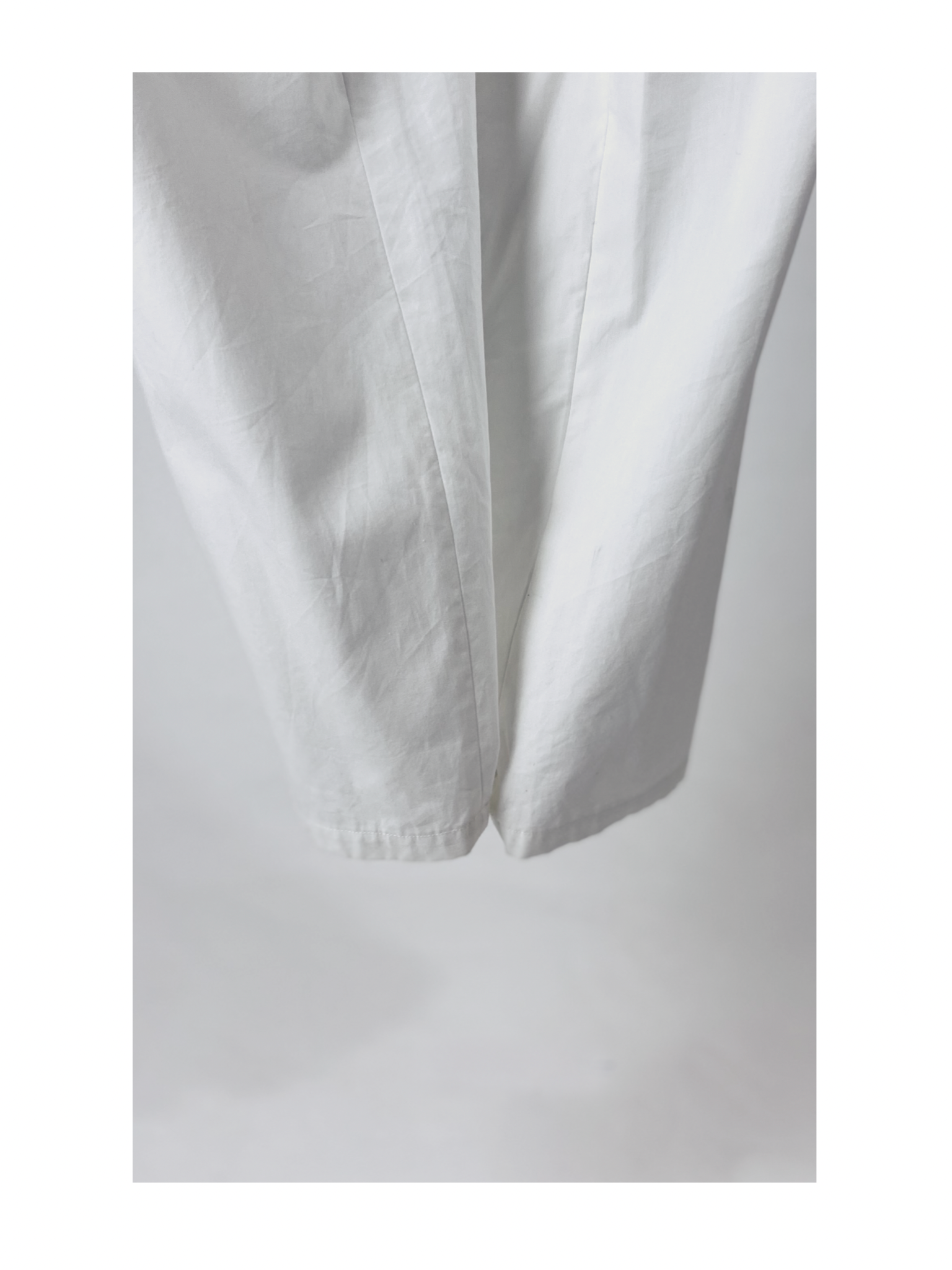 Close-up of a pair of white pants with a soft fabric texture, hanging vertically against a light gray background. The focus is on the fabric folds and stitching details.