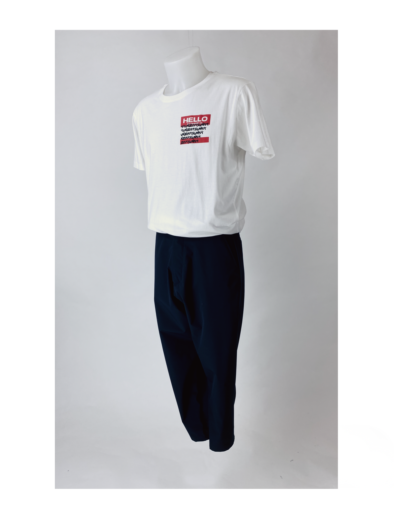 White short-sleeve T-shirt with a red and black Hello My Name Is name tag design, paired with dark blue pants, displayed on a mannequin against a plain background.