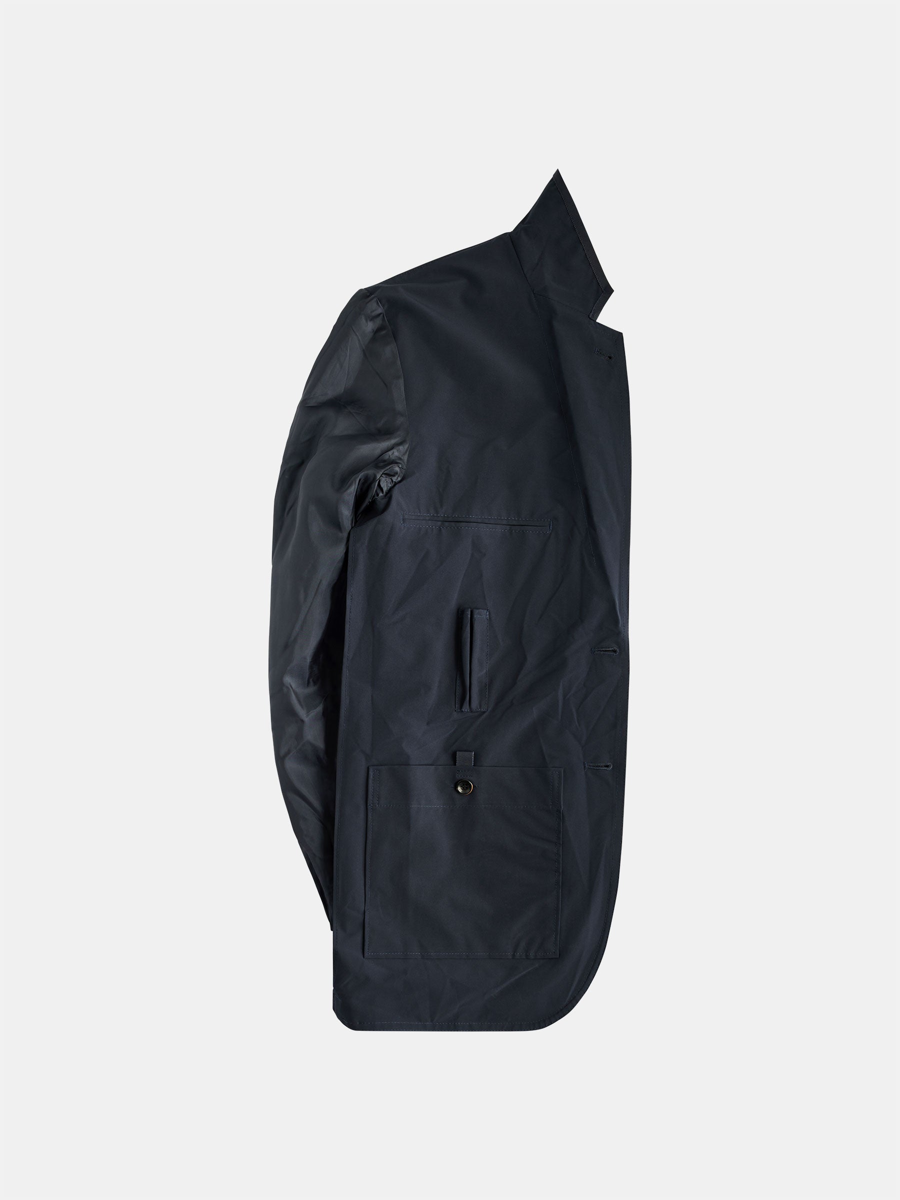 A side view of the sleek, dark-colored Original POCKETPARACHUTE® Travel Blazer Navy by gabrielstunz showcases its high collar and buttoned pockets against a neutral background. This minimalist design is crafted from soft, shiny material and features a water-repellent, packable design for ultimate convenience.