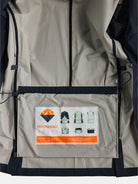 The image provides a glimpse into the interior of a gabrielstunz Original POCKETPARACHUTE® Travel Blazer in Navy, featuring a pocket with the iconic label. Diagrams demonstrate its packable design and transformation process, while accompanying text and an orange umbrella icon emphasize its water-repellent property.