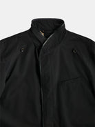 The POCKETPARACHUTE® Raincoat by gabrielstunz is a dark-colored jacket with a high, button-up collar and zipper closure, designed for easy packing. It comes with grommet details on the chest and a single chest pocket. The lightweight and sleek fabric is water-repellent, ideal for unexpected showers.