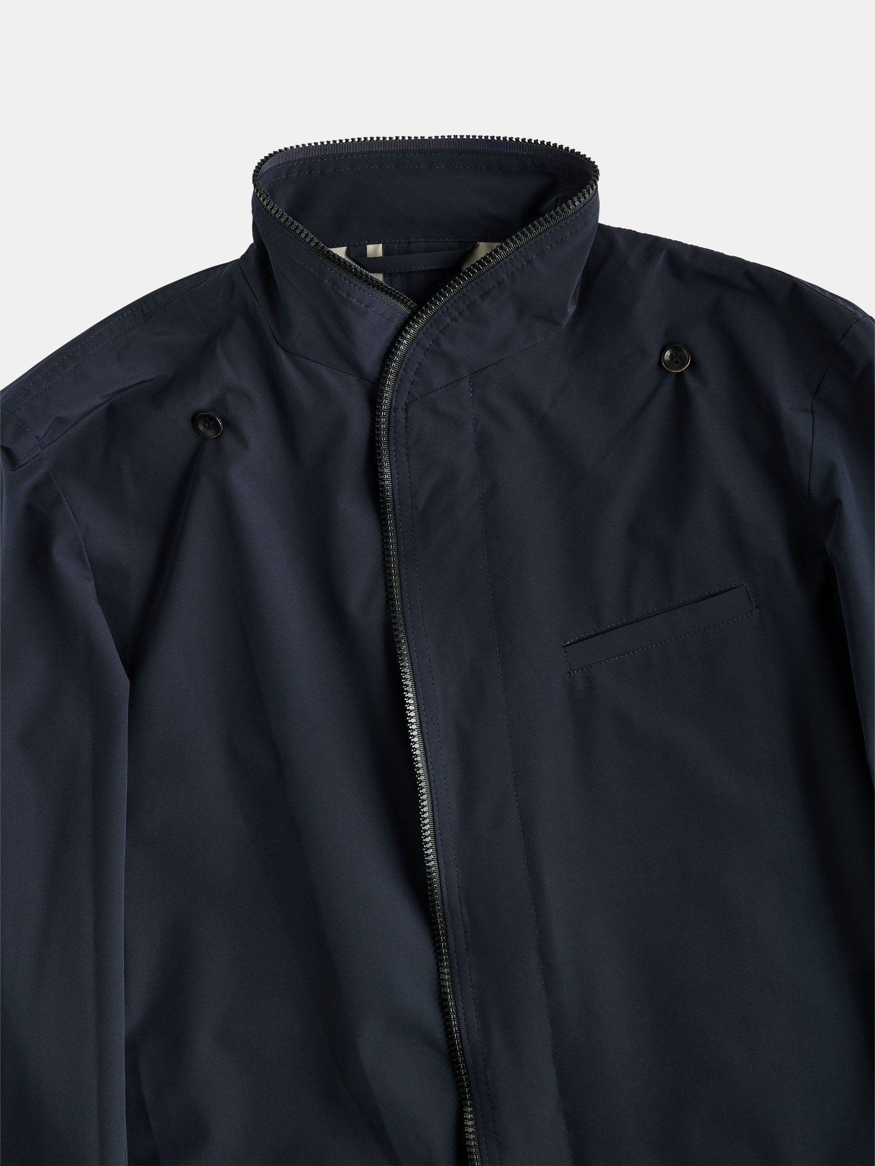 Introducing the gabrielstunz POCKETPARACHUTE® Tech Raincoat: This navy raincoat features a zipper closure and high collar, complemented by two button details near the shoulders and a small chest pocket. Displayed against a light gray background, this stylish piece is crafted from innovative fabric for packable convenience, making it perfect for versatile wear.