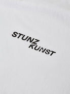 Close-up of a white fabric crafted from organic cotton, featuring the text "STUNZ BY KUNST" printed in black with a modern, sans-serif font. This piece from gabrielstunz's STUNZISTKUNST Edition T-Shirt collection emphasizes the use of sustainable fabrics that offer both smoothness and a slight texture.